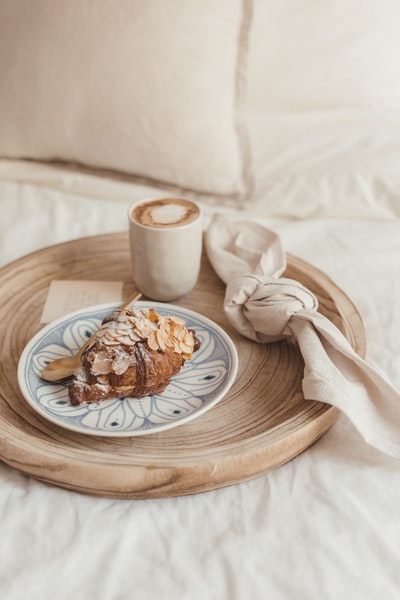 棕色的面包放在棕色的木制桌子上白色的陶瓷杯旁边的白色陶瓷盘上